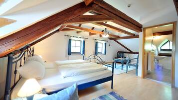 Ein Schlafzimmer mit Bett, Nachttischlampe, Holzbalken, einem Fenster und einem Badezimmer mit Waschbecken.