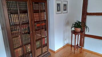Ein Zimmer mit einer Holzhütte voller Bücher, einem kleinen Holztisch mit einem Blumentopf und zwei gerahmten Bildern an der Wand.