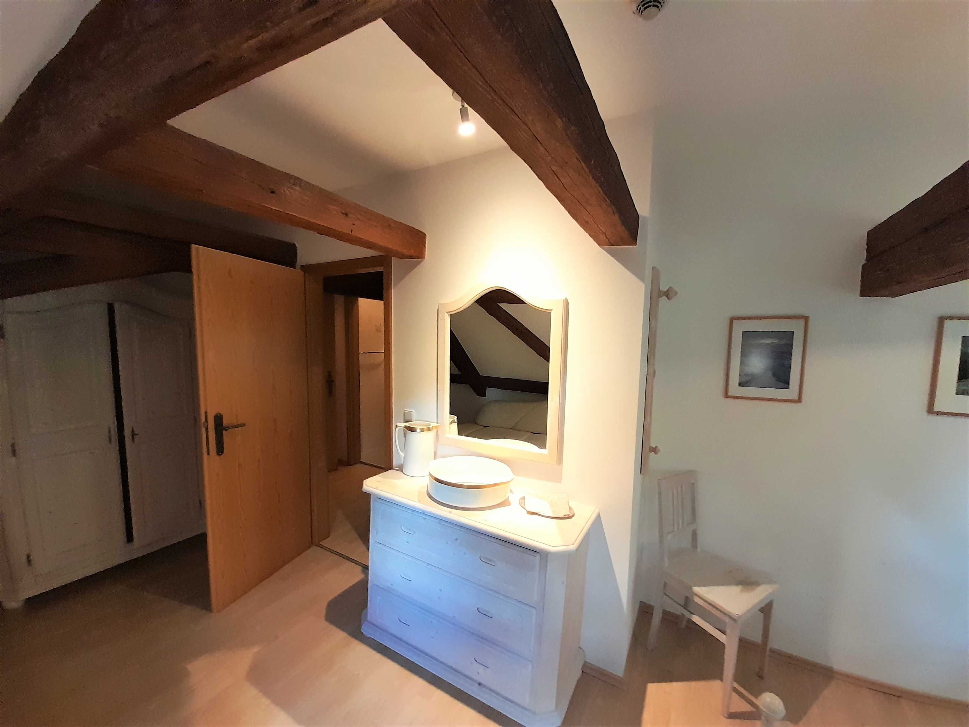 A room with a white dresser, a mirror, and a small table. There is a door leading to another room.