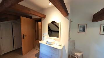 A room with a white dresser, a mirror, and a small table. There is a door leading to another room.