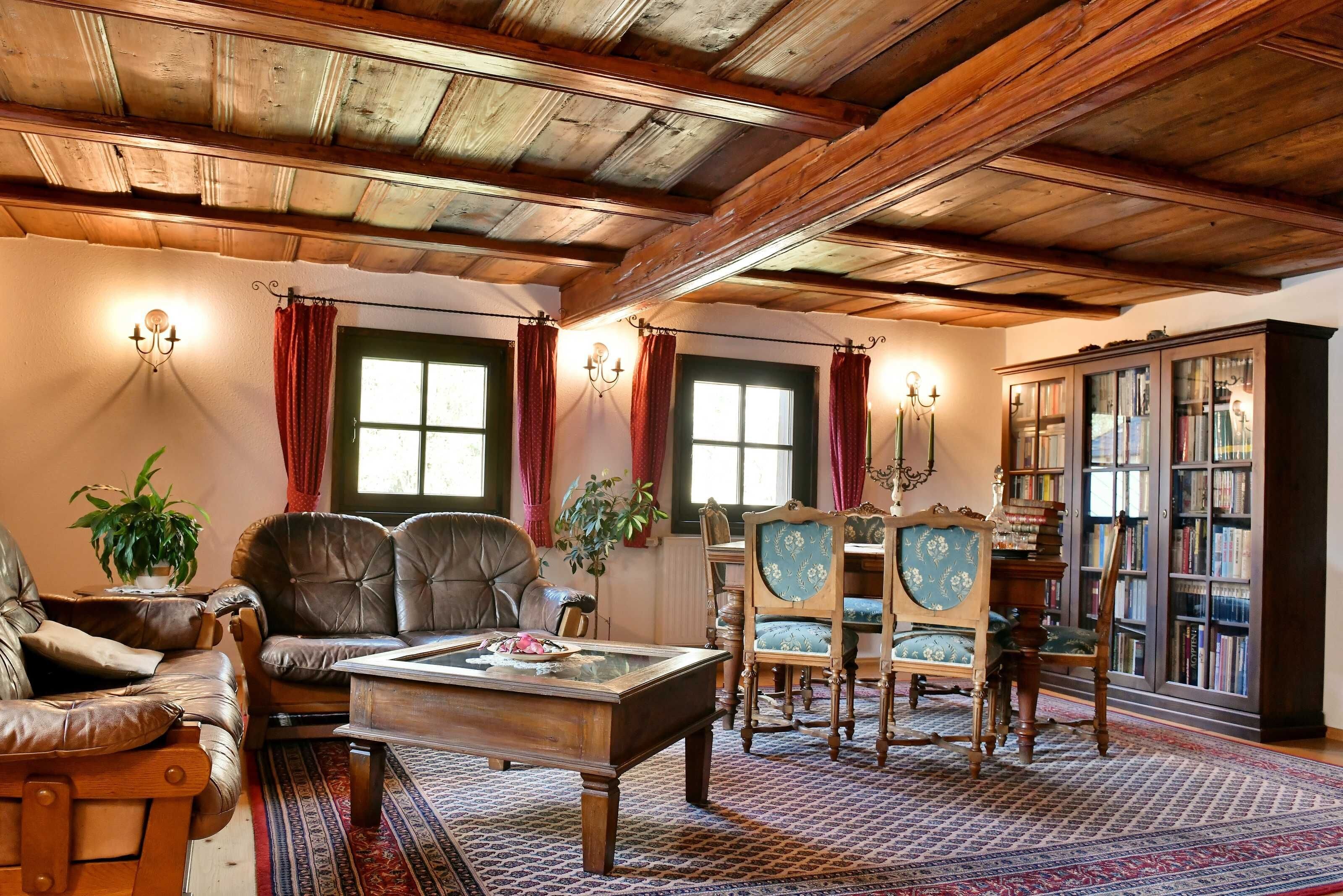 A traditional room with a wooden ceiling, leather chairs, a wooden coffee table, and a bookshelf.