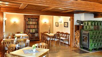 A cozy library with wooden bookshelves and tables, a fireplace, and a ceiling with exposed beams.