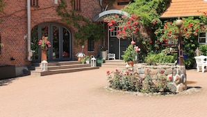 A courtyard with a brick building, stone steps, and a white chair. - Der Besitz 6a (Stoltebuell)
