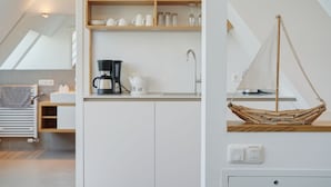 A modern kitchen with white cabinets, a wooden shelf with dishes, a coffee maker, and a small sailboat decoration. - Der Besitz 6a (Stoltebuell)