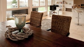 Uma sala de jantar com uma mesa de madeira, duas cadeiras de vime, um castiçal de vidro e uma decoração de corda.