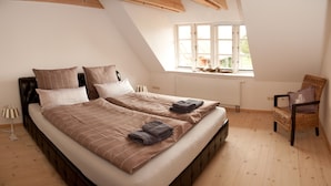 Quarto com teto estilo loft, cama com cabeceira, uma cadeira e janela com vista para o exterior.