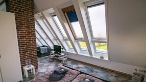 Een kamer met een schuine hemel, dakramen, een bed, een televisie en een klein tafeltje met een glas.