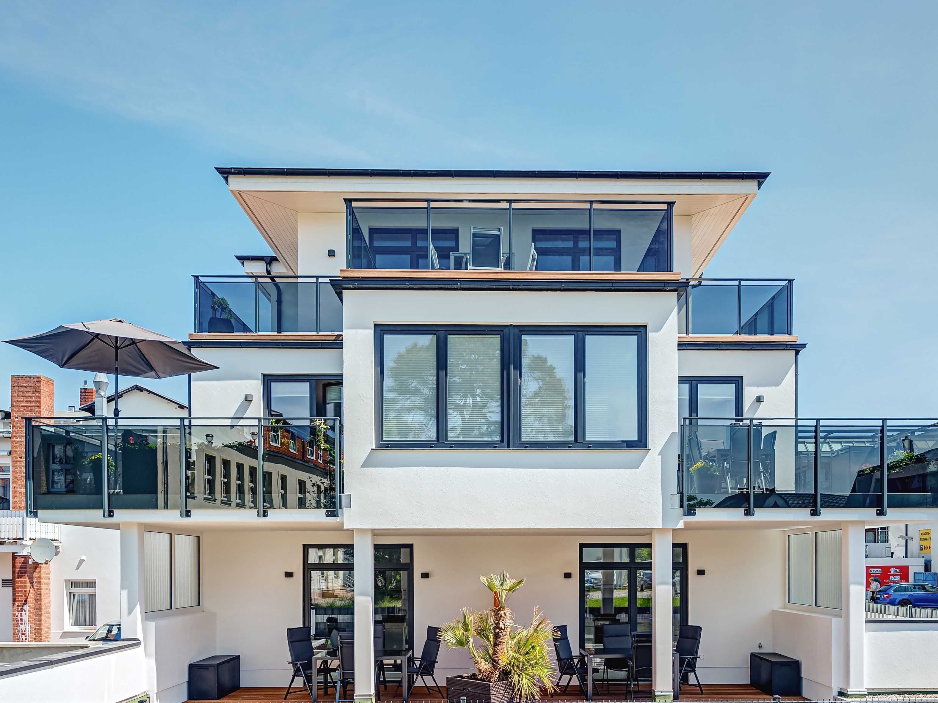 Ein modernes, zweistöckiges Gebäude mit großen Fenstern, einem Balkon und Außenbestuhlung.