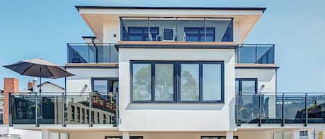 A modern two-story building with large windows, a balcony, and outdoor seating.