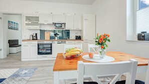 A modern kitchen with white cabinetry, a microwave, and a dining area with a wooden table and white chairs.