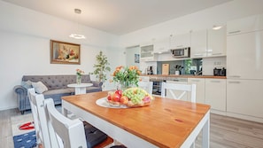A modern kitchen with white cabinets, a dining table with chairs, and a fruit bowl.