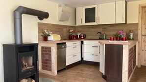 A compact kitchen with a wood-burning stove, white cabinets, and a wooden countertop. - Ferienhaus Vietgest, Deutschland (Lalendorf)