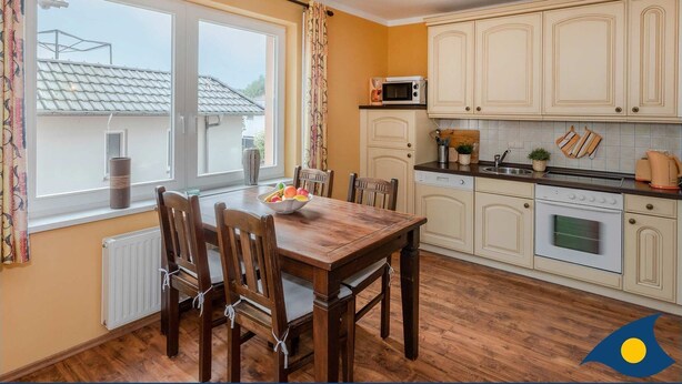 A compact kitchen with a dining area, featuring a wooden table and chairs, a microwave, and a stove. - Vacation apartment at Krebssee Whg. Otter - Otter (Heringsdorf)