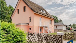 A two-story house with a thatched roof, a balcony, and a wooden fence. - Vacation apartment at Krebssee Whg. Otter - Otter (Heringsdorf)