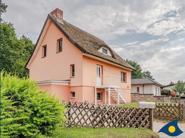 A pink house with a thatched roof, a wooden fence, and a mailbox.