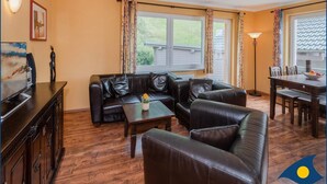 A living room with a leather sofa, a coffee table, and a dining area with a table and chairs. There is a TV on a cabinet, and a lamp is visible. - Vacation apartment at Krebssee Whg. Otter - Otter (Heringsdorf)