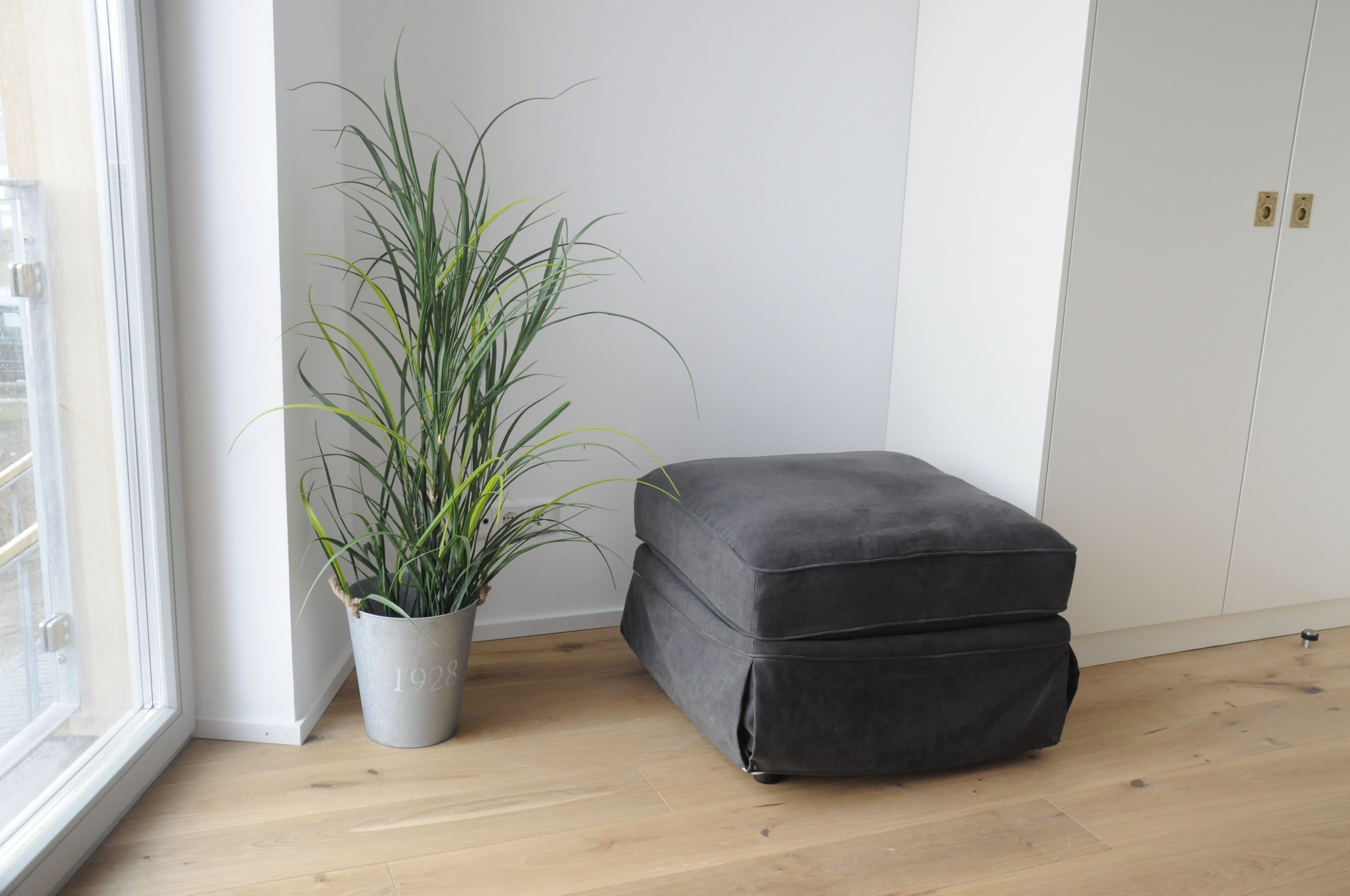 Una habitación con un banco tapizado gris, una planta en maceta y un armario blanco.