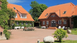 A courtyard with brick buildings, outdoor seating, and a small garden. - Das Neuhaus (Stoltebuell)
