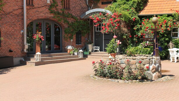 A courtyard with a brick building, stone steps, and a white chair. - Das Neuhaus (Stoltebuell)
