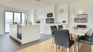 Una cocina moderna con armarios blancos, una isla central y una zona de comedor con una mesa blanca y sillas negras.