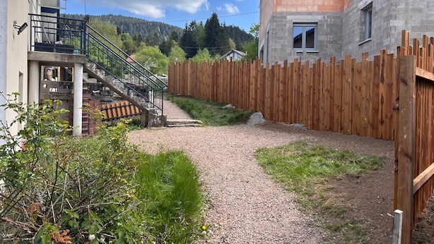Un quartier résidentiel avec un chemin de gravier, une clôture en bois et un bâtiment doté d’un escalier.