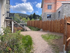 A residential area with a gravel path, wooden fence, and a building with a staircase. - Les Coteaux II (Gérardmer)