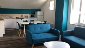 Un salon moderne avec un canapé bleu, une table basse blanche et un coin repas comprenant une table blanche et des chaises bleues.