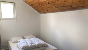 Un petit lit, bien fait, dans une pièce aux murs blancs et au plafond en bois.