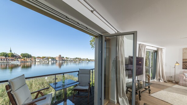 A balcony with a view of a river and cityscape, furnished with a table, chairs, and a sofa. - Kapitänsbrücke - Penthouse (Kappeln)