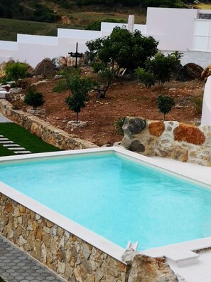 A swimming pool with a stone border, surrounded by a landscaped garden with small trees and shrubs. - Feather House FH Lace (São Bartolomeu de Galegos)