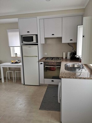 A compact kitchen with a built-in microwave, a gas stove, and a sink. - Feather House FH Lace (São Bartolomeu de Galegos)