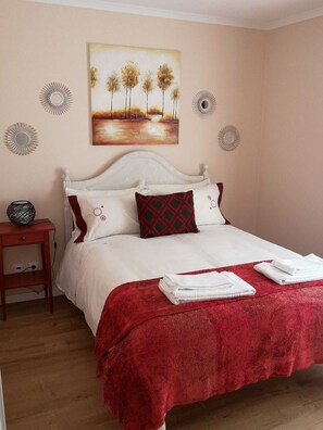 A neatly made bed with white bedding and a red throw blanket, a painting of trees on the wall, and a small bedside table with a lamp. - Feather House FH Lace (São Bartolomeu de Galegos)
