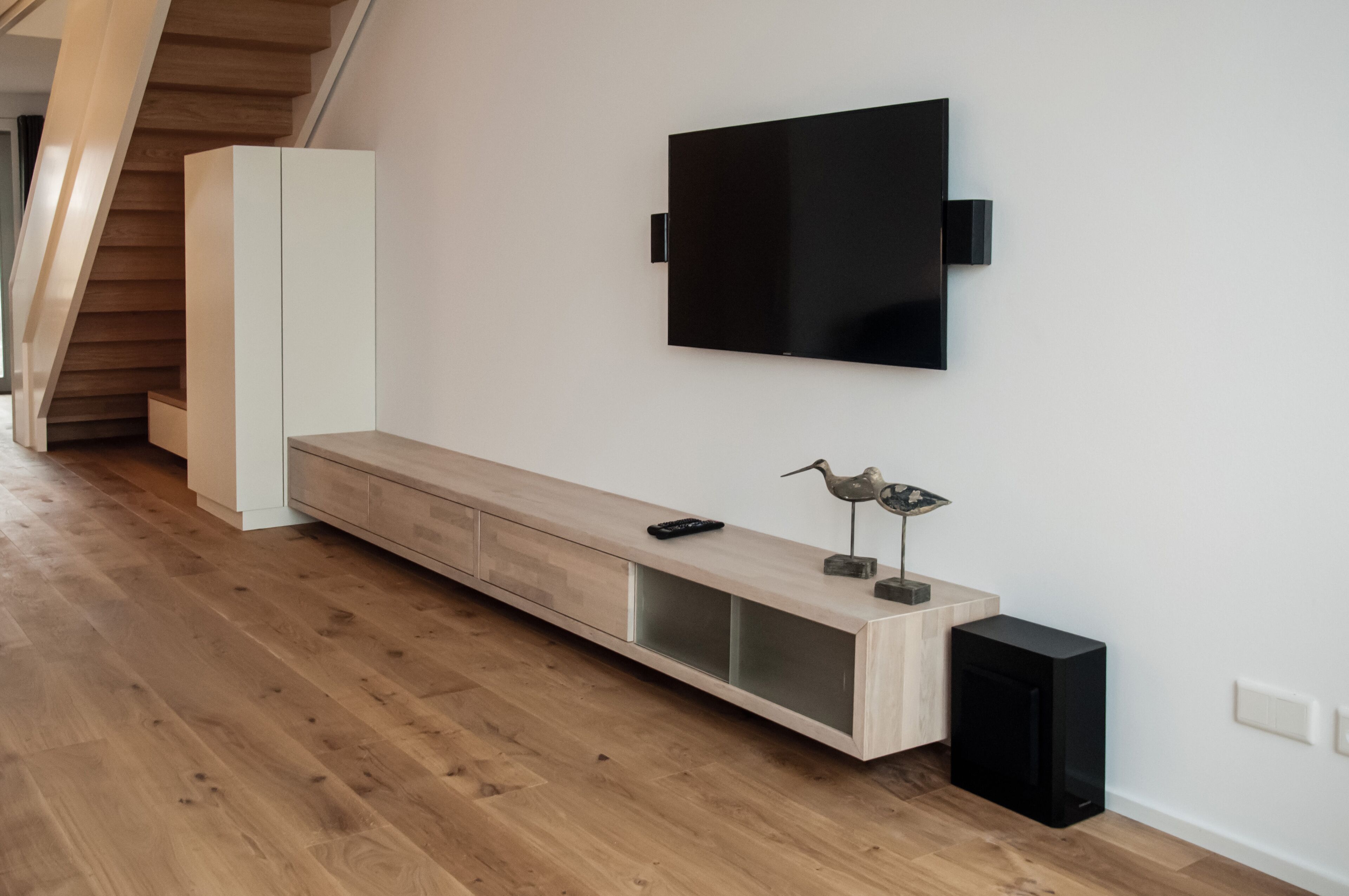 Un salon moderne avec un banc en bois, un téléviseur à écran plat fixé au mur et une petite enceinte.