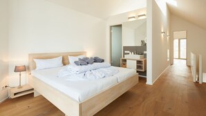 Une chambre moderne avec un lit en bois, une table de chevet avec une lampe, une armoire intégrée et une salle de bain avec un miroir et un lavabo.