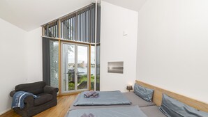 A modern bedroom with two beds, a sofa, and a large sliding glass door leading to a balcony. - Seglerwohnung 9 (Kappeln)