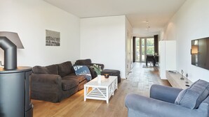 A modern living room with a sofa, a coffee table, and a fireplace. There is a television mounted on the wall and a dining area in the background. - Steuermann (Kappeln)