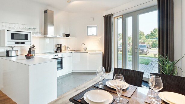A modern kitchen with a central island, white cabinetry, and a dining area with a table set for two. - Steuermann (Kappeln)