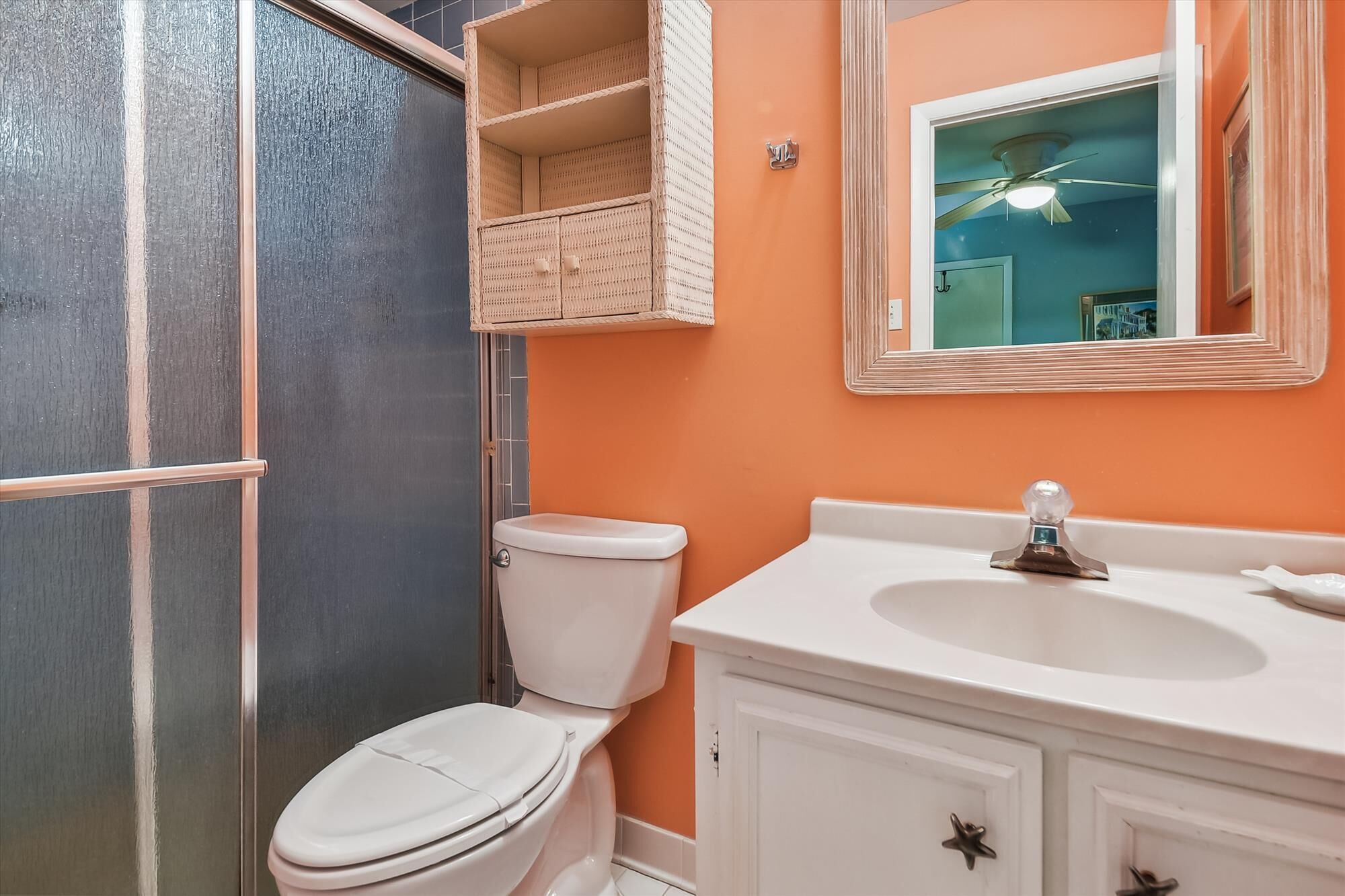 Une salle de bain avec des toilettes blanches, un lavabo blanc et un miroir au-dessus du lavabo.
