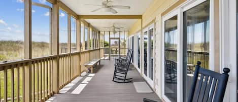 A covered porch with a view of the beach, wooden benches, and a ceiling fan.