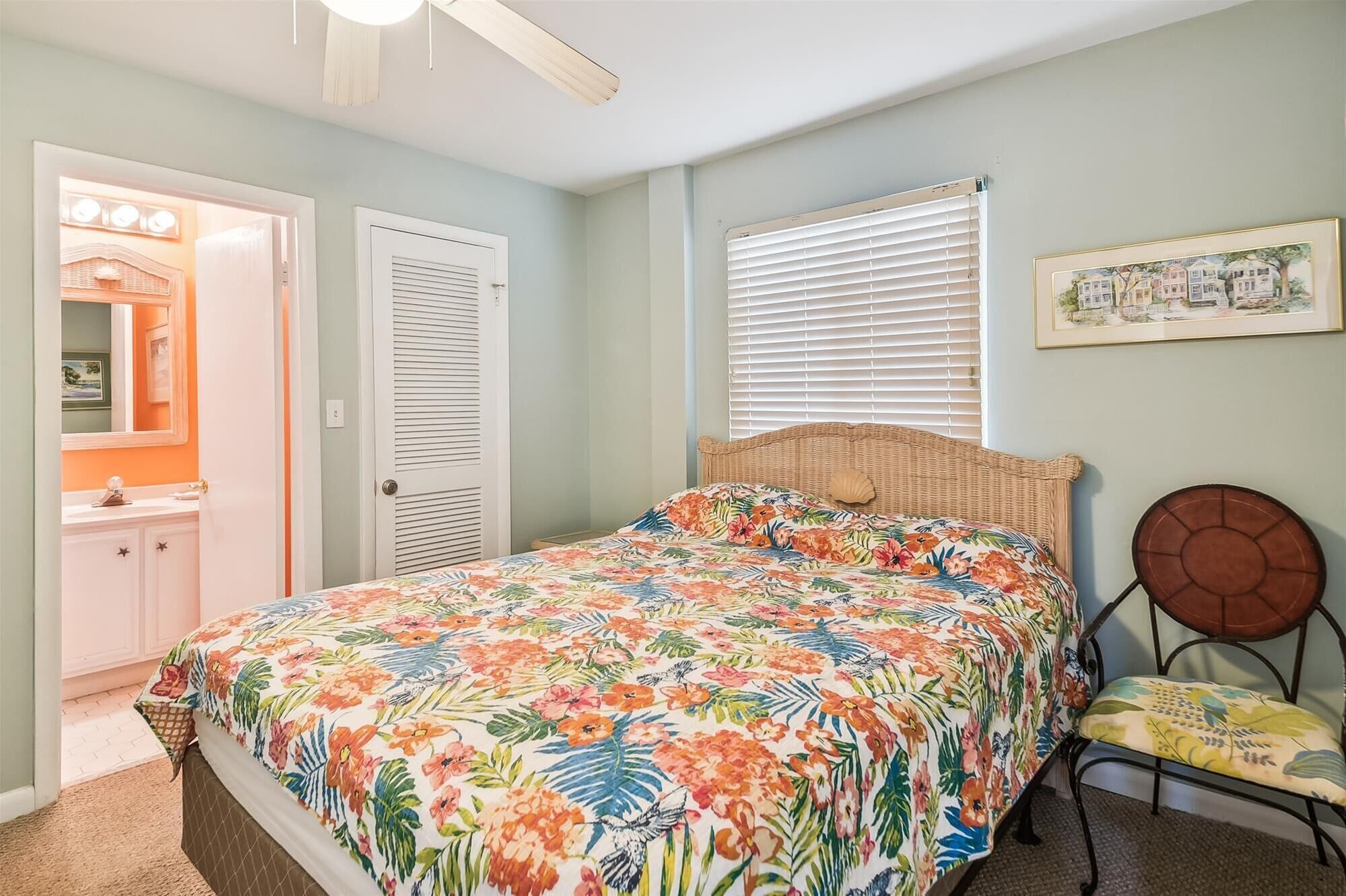 Une chambre à coucher comprenant un lit, une chaise, une fenêtre avec des stores, une porte et un ventilateur de plafond.