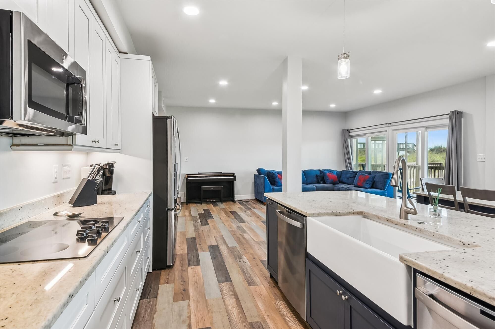 Une cuisine moderne dotée d’un îlot central, d’appareils électroménagers en acier inoxydable et d’un parquet en bois disposé en chevrons.