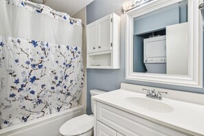Un baño con un lavamanos blanco, un espejo, un inodoro y una cortina de ducha con motivos florales.