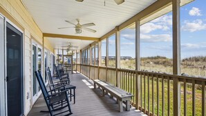 Eine überdachte Veranda mit Holzbanken und Stühlen, einem Deckenventilator und Blick auf den Strand.
