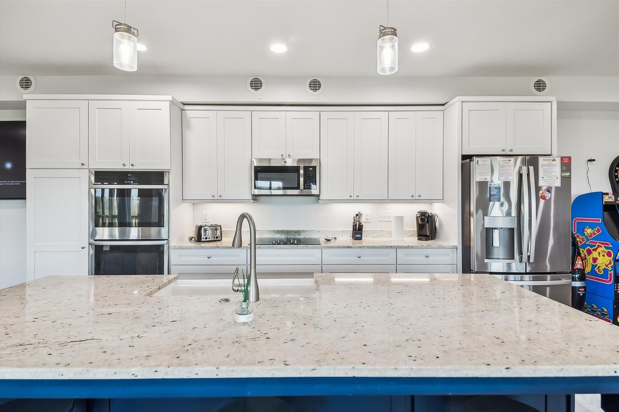 A modern kitchen with white cabinets, stainless steel appliances, a granite countertop, and pendant lighting.