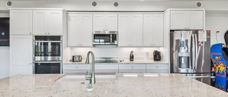 A modern kitchen with white cabinets, stainless steel appliances, a granite countertop, and pendant lighting.