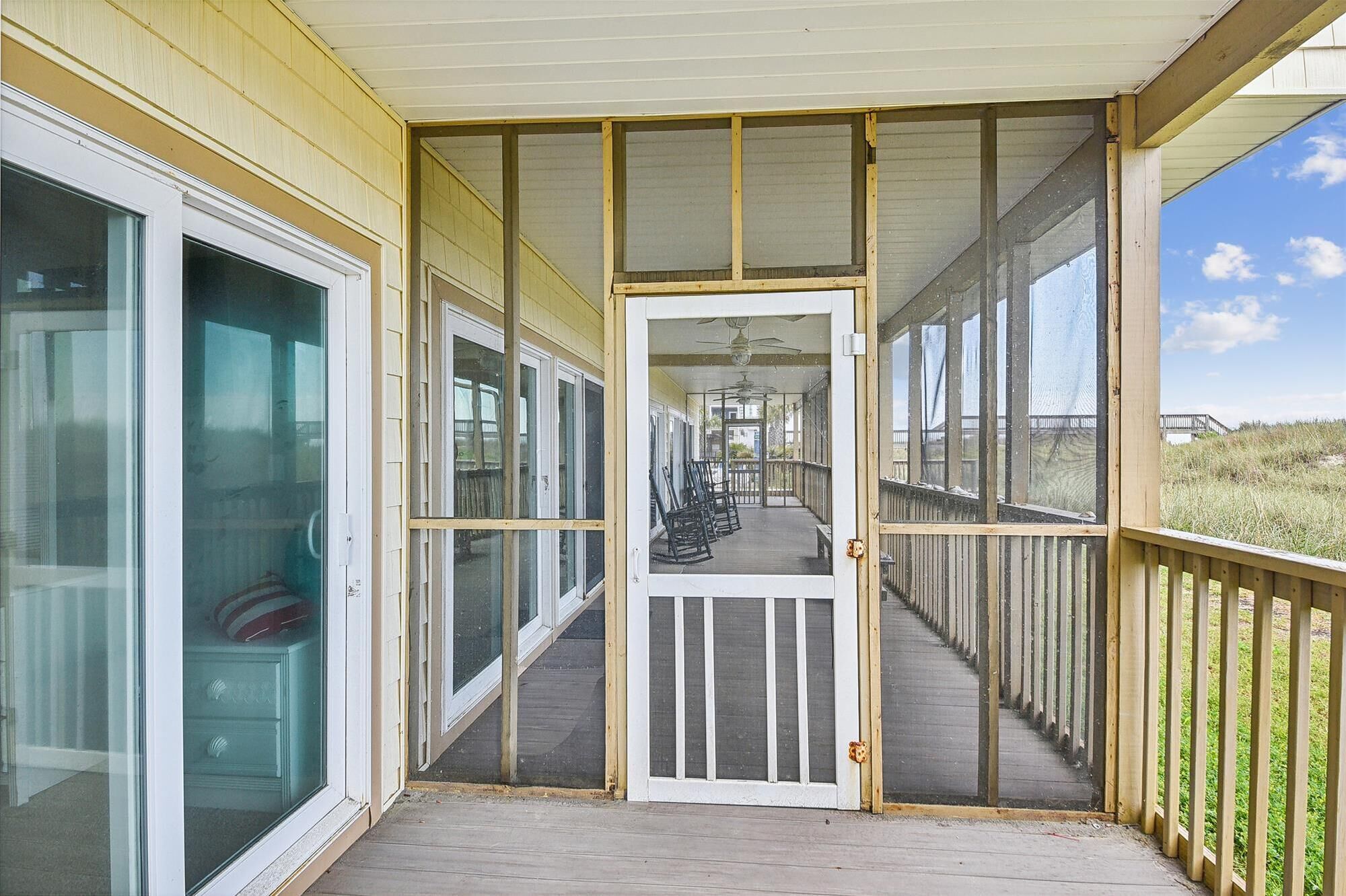 A covered porch with a wooden deck, glass doors, and a view of the beach.