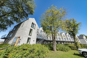 A modern building with a grey brick facade, multiple balconies, and a tree in the foreground. - Lotsenhaus 11 (Kappeln)