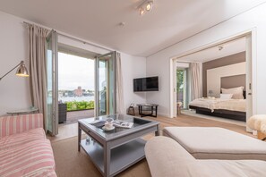 A modern hotel room with a large bed, a TV, a glass coffee table, and a balcony with a city view. - Lotsenhaus 11 (Kappeln)