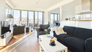 Una sala de estar moderna con un ventanal grande, un sofá negro, una mesita de centro blanca y un televisor.