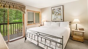 A bedroom with a bed, two bedside tables, a window with blinds, a painting on the wall, and a view of greenery outside. - Ski OR Walk to Lifts, Village and Hot Tub! Luxurious & Clean Beaver Creek Condo (Beaver Creek)